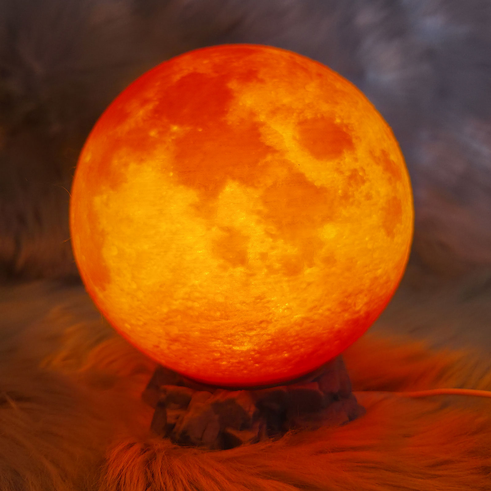 Eingeschaltete 3D-gedruckte Mondlampe auf einem Felssockel mit warmem orange-rotem Farbverlauf